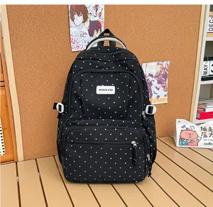 Vue de face du sac noir, avec pois blancs, plusieurs poches zippées et une petite étiquette.
