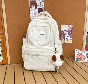 Vue de face d’un sac à dos blanc à pois, avec poches zippées et petit pendentif chien en peluche