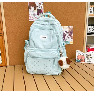 Vue d’un sac à dos bleu clair à pois, avec poches avant et pendentif de chien en peluche