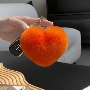 Primer plano de un corazón de peluche naranja y suave, con cadena dorada, sostenido en la mano