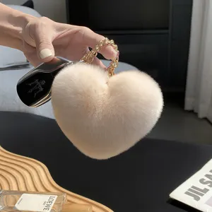 Primer plano de un corazón de pelo color marfil con cadena dorada, sostenido ante fondo oscuro