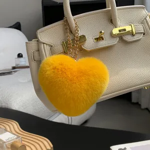 Adorno de corazón amarillo y mullido, con cadena dorada, colgado de un bolso color crema en interior