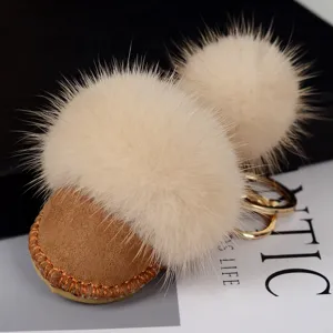 Gros plan sur un pompon ivoire, une base en daim brun, des coutures orange et un anneau métallique