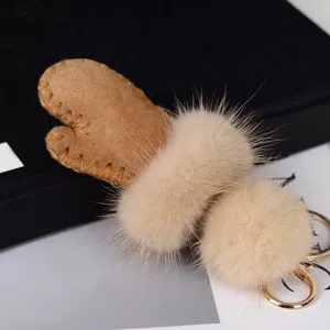 Gros plan sur un pompon beige, une pièce en daim camel avec couture apparente et un crochet doré