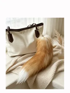 Faux fox-tail plush charm with gold hook hanging from a cream handbag in a cozy home setting