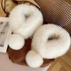 Overhead view of two white fluffy fur collars with round pom-poms arranged on a brown suede bag