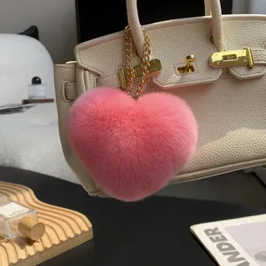 Primer plano de un suave colgante rosa en forma de corazón, con cadena dorada, en un bolso beige