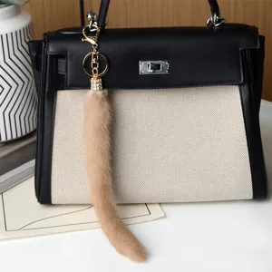 Dettaglio di un ciondolo con coda in pelliccia beige e terminale dorato con strass su una borsa