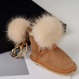 Gros plan sur un pendentif botte en suédine brune, pompon crème, coutures orange et mousqueton doré