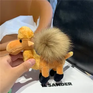 Close-up of a tan plush camel charm with a fluffy brown hump pompom and dark feet, held by hand