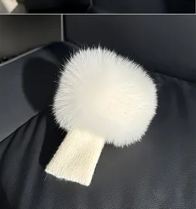 Close-up of a white fluffy pom-pom attached to a cream ribbed knit strip on black leather