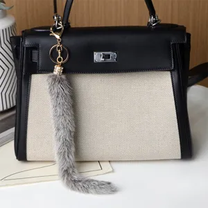 Ciondolo grigio e soffice con dettaglio in strass e gancio dorato, appeso a una borsa bicolore.