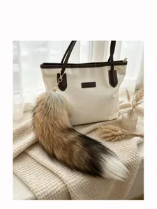 Fox-tail fur charm with brown, dark brown and white tips, attached to a tote by a gold clasp