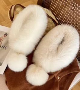 Flat lay of two ivory faux-fur scarves with fluffy pom-pom ends on warm-toned styling props