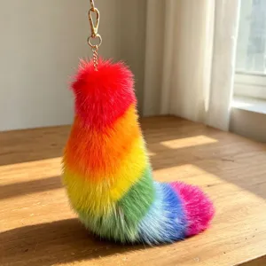 Close-up of a fluffy rainbow faux-fur tail charm with gold-tone chain and hook on wood