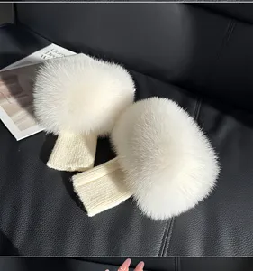 Close-up of two white fluffy pom-pom cuffs with cream ribbed knit bands displayed on a dark seat