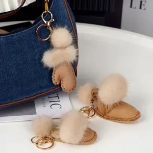 Détail des pompons en fausse fourrure beige et des breloques en forme de botte avec crochets dorés