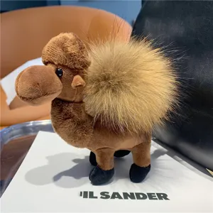 Close-up of a brown plush camel with a fluffy tan hump and dark feet, displayed on a white board