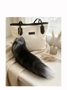 Silver fox tail charm with a gold metal clasp hanging from a cream tote bag by a window