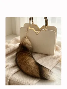 Close-up of a brown-to-dark-brown furry tail charm with a gold chain on a cream handbag