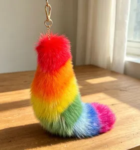 Close view of the rainbow-colored fluffy tail charm, gold-tone chain and clasp on a wooden table