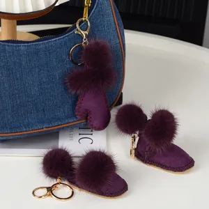 Gros plan sur des breloques violettes en forme de bottine, avec pompons doux et crochets dorés