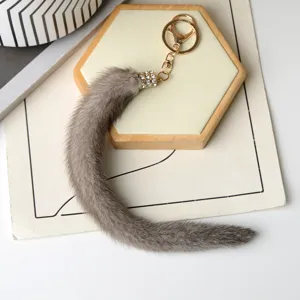 Coda di peluche grigia su fondo bianco, con chiusura dorata e manicotto decorato con strass