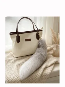Close-up of a gray-white fluffy tail charm with a gold clasp beside a cream tote bag