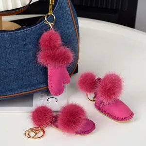 Trois breloques roses, gant et bottes à pompons doux, avec clips dorés près d’un sac en jean