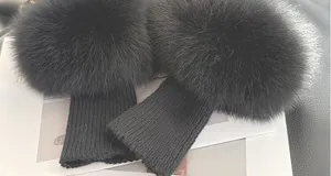Close-up of two dark charcoal ribbed knit wrist warmers with fluffy cuffs, laid flat on a surface