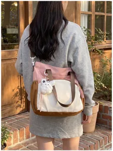 Vue de dos d’un sac en tissu rose, crème et brun, avec bandoulière tissée et breloque ourson