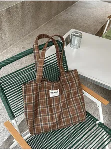 Brown plaid fabric bag with a white BEAUT hand made label, resting on a green woven outdoor chair
