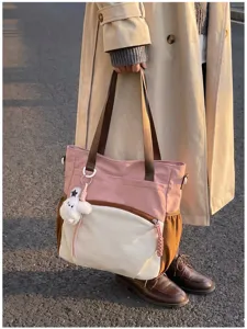 Vue de rue d’un sac rose et crème, avec anses brunes, poche zippée et petit pendentif en peluche.