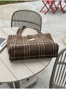 Brown plaid fabric and small white label on a tote bag displayed on an outdoor table