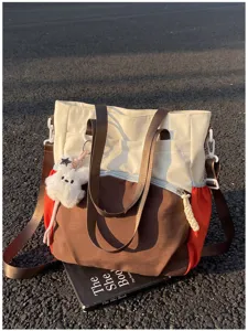 Sac à panneaux crème, bruns et rouge orangé, avec sangles et peluche ourson sur l’asphalte