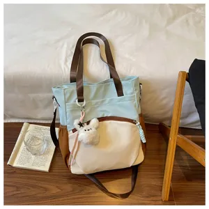 Un sac bicolore bleu clair et ivoire, avec bordures brunes, poche zippée et pompon lapin