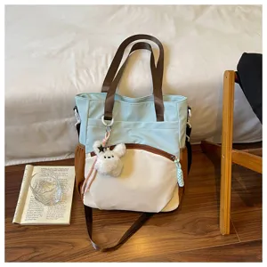 Sac bleu et blanc avec bandoulières brunes, poche zippée à l’avant et petit ourson en peluche