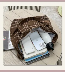 Overhead view of an open brown plaid bag with gray lining, phone, tablet, books and bottle