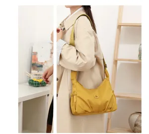 Vue en situation d’un sac en nylon jaune moutarde froncé, à large bandoulière, porté sur l’épaule