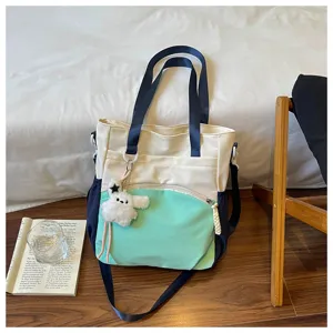 Sac crème et vert menthe avec anses bleu marine et breloque ourson, présenté sur une table en bois