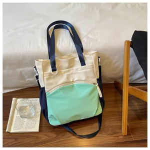 Sac crème, bleu marine et menthe avec poche zippée sur le devant, posé près d’un livre en intérieur