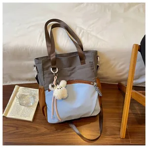 Sac gris et bleu clair, détails bruns et petit lapin en peluche, posé sur un sol en bois clair