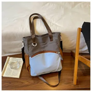 Sac bicolore taupe et bleu clair, avec bordure brune, anses tissées et poche zippée à l’avant