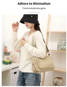 Sac beige en nylon à plusieurs compartiments, avec bandoulière réglable, porté sur un pull clair.