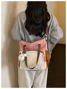 Vue de dos d’un sac rose, crème et brun, porté à l’épaule avec un ourson en peluche