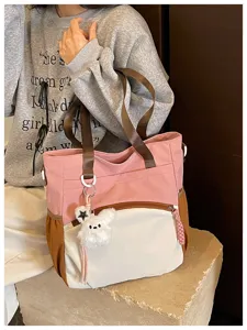 Vue d’un sac rose et blanc, avec de larges anses brunes et un pendentif lapin tout doux.