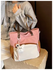 À l’épaule, le sac montre des panneaux roses, blancs et bruns, un lapin en peluche et un pompon.