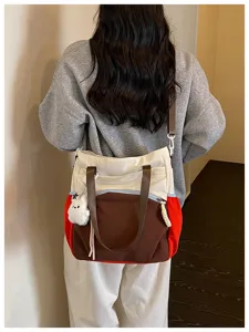 Vue arrière d’une personne portant un cabas écru, marron et rouge avec un pendentif peluche blanc
