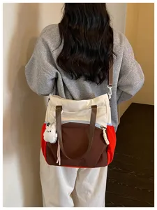 Vue de dos d’une personne portant un sac écru, brun et rouge avec un petit pendentif en peluche