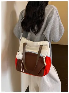Vue arrière d’un sac porté à l’épaule, avec anses brunes, panneaux rouges et breloque en peluche